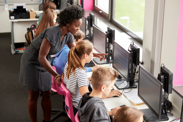 A teacher helping pupils use classroom computers, highlighting how managed print services for schools can reduce costs, improve efficiency and support more secure printing.