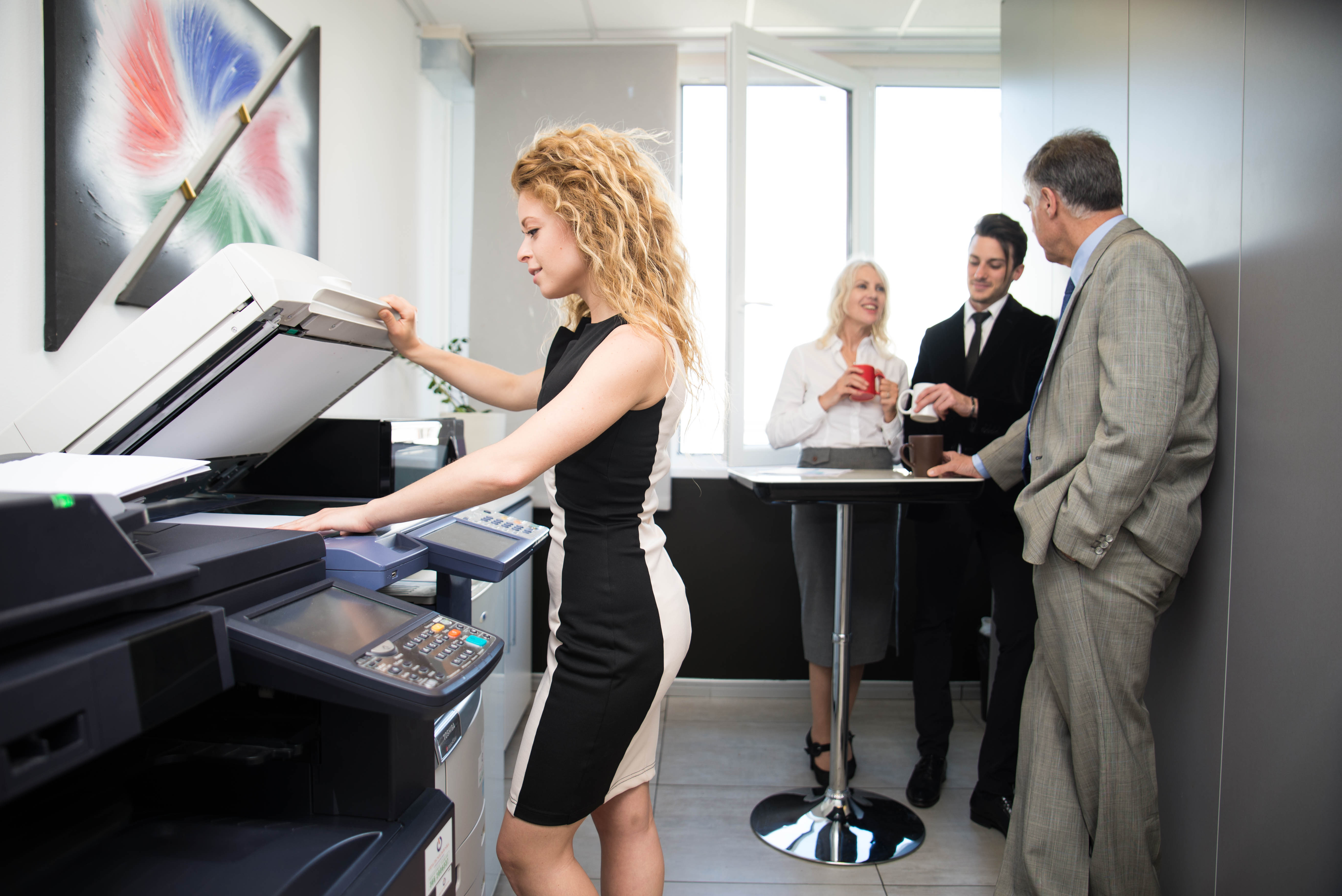 Office worker handling documents on a multifunction printer, highlighting the security risks and hidden costs of unmanaged office printing.