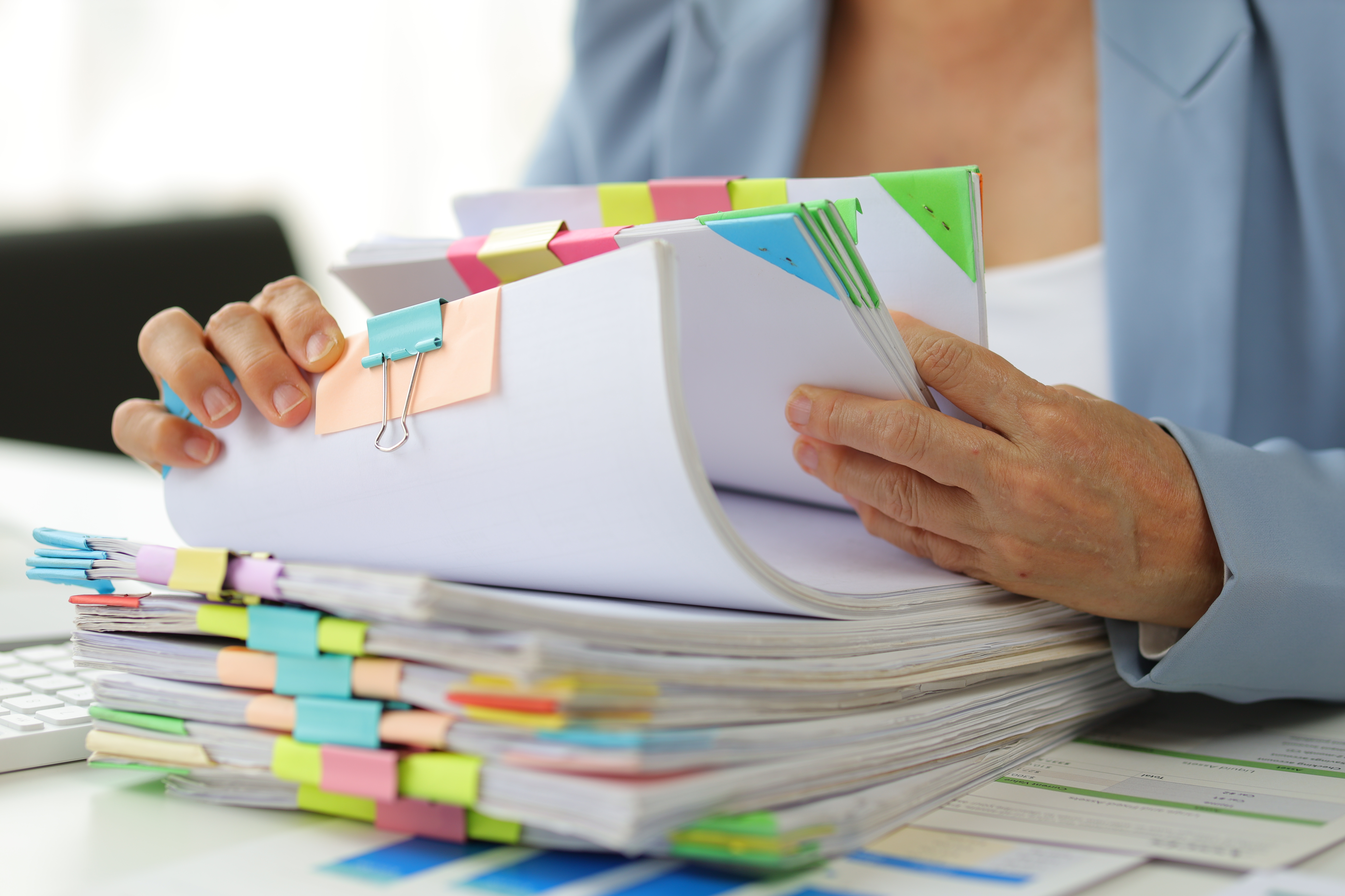 Person searching through stacks of paper files, highlighting lost documents, slow approvals and compliance risks caused by outdated document management.